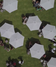 An aerial view of wedding guests at tables under white umbrellas.